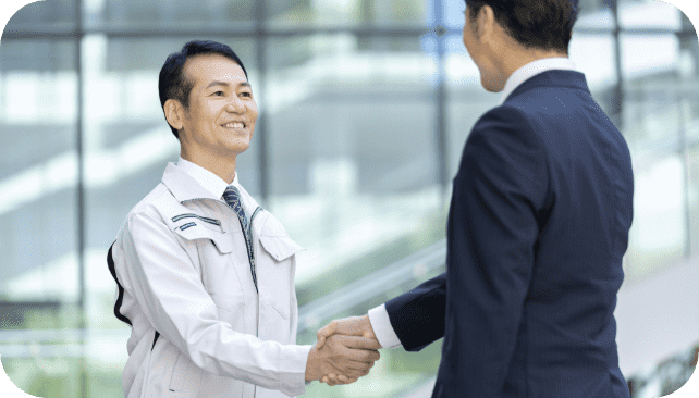 会社の外で握手をする作業員とスーツの男性